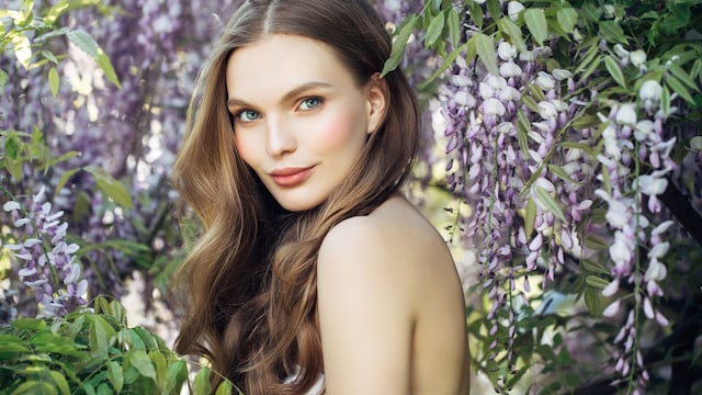 Rostro de mujer con piel clara y pelo largo, rodeada de flores