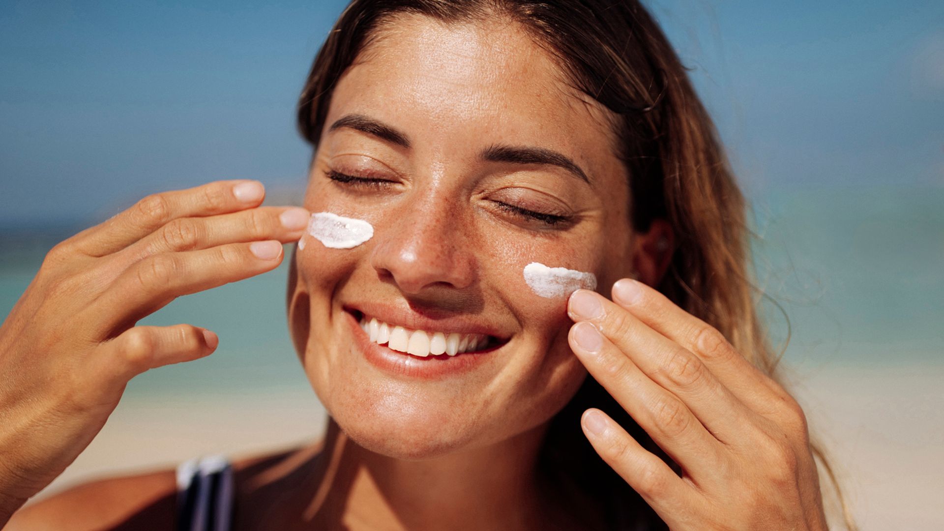 Una mujer sonriente poniéndose protección solar en la playa