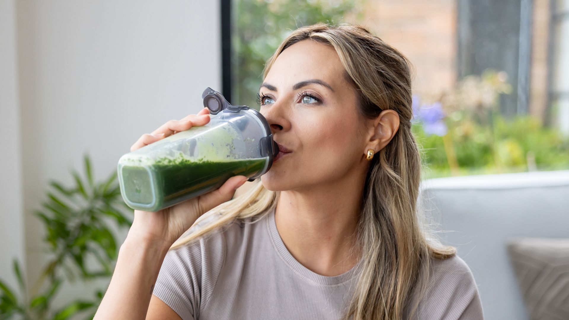 Mujer joven rubia tomando un batido verde en su salón