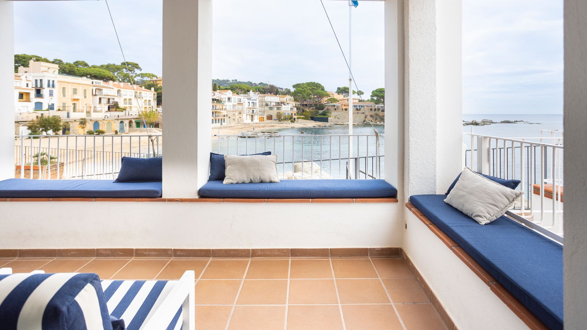 Terraza de estilo marinero con bancos, almohadones azules, suelo porcelánico y vistas al mar