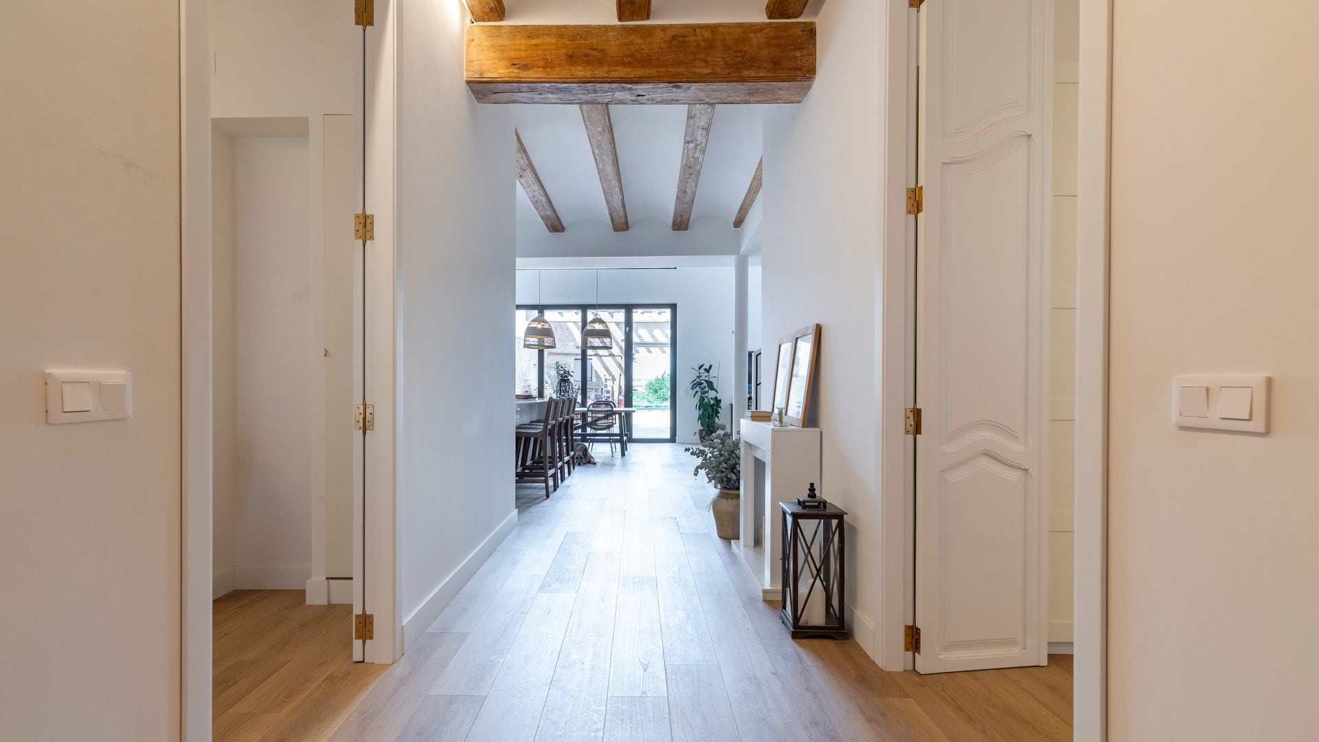 Pasillo con suelo de madera, puertas a los lados blancas con molduras, vigas en el techo y comedor