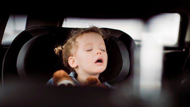 Niña pequeña durmiendo con la boca abierta en el asiento trasero de un coche, vista desde el retrovisor.