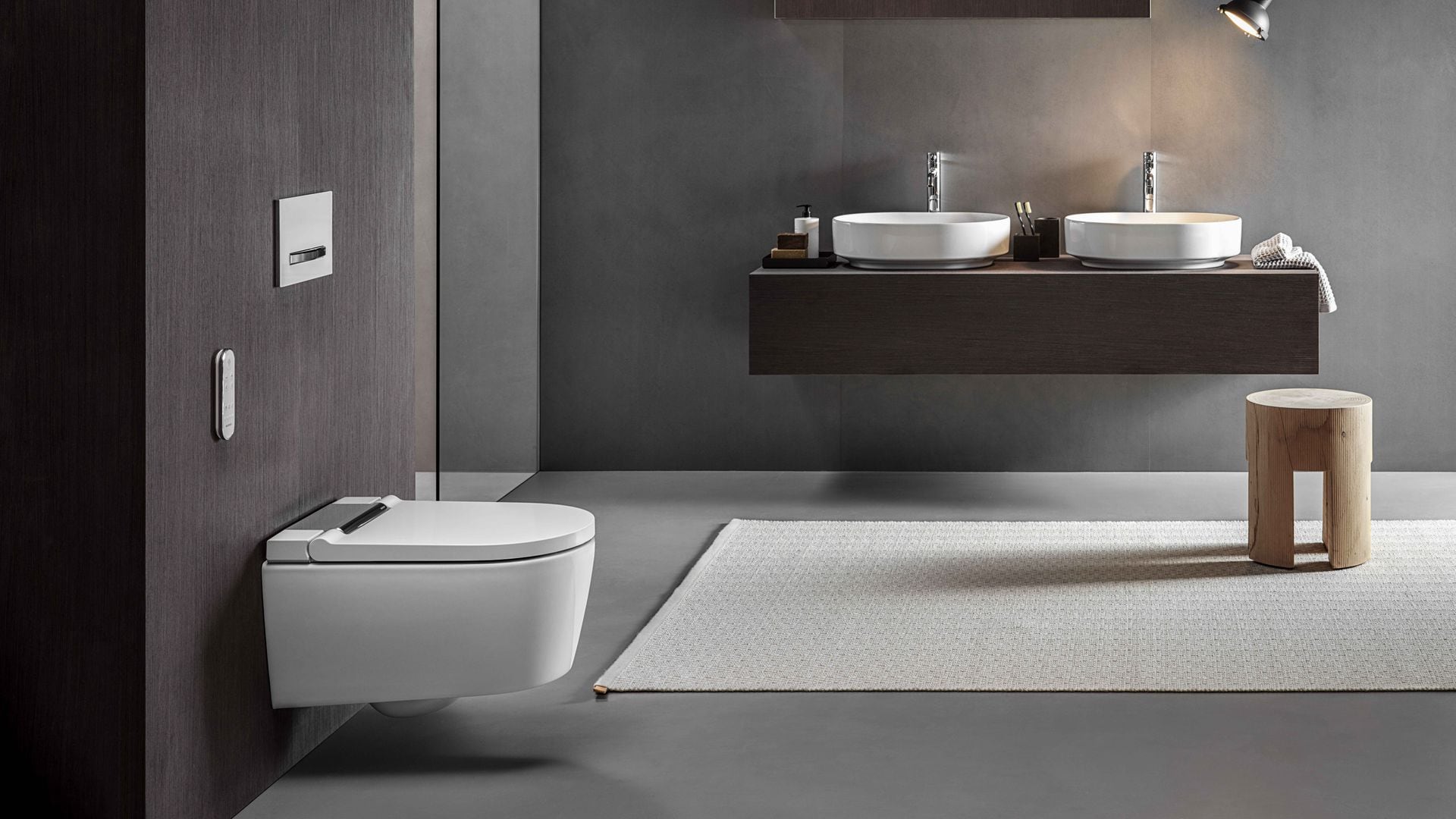 Baño con paredes en gris, sanitario suspendido, alfombra, mueble bajolavabo suspendido, lámpara de techo, taburete