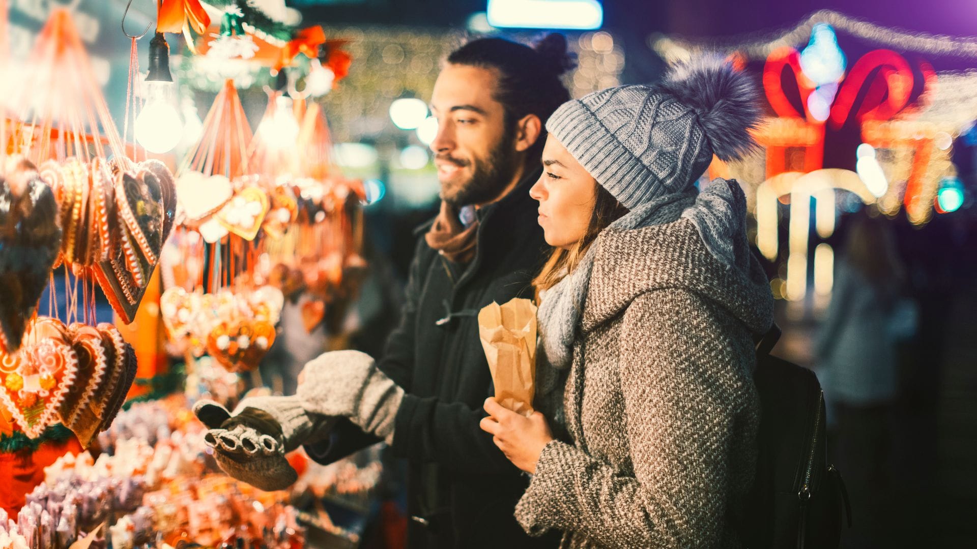 Pareja joven en un mercadillo navideño europeo, mirando un puesto de artesanía.