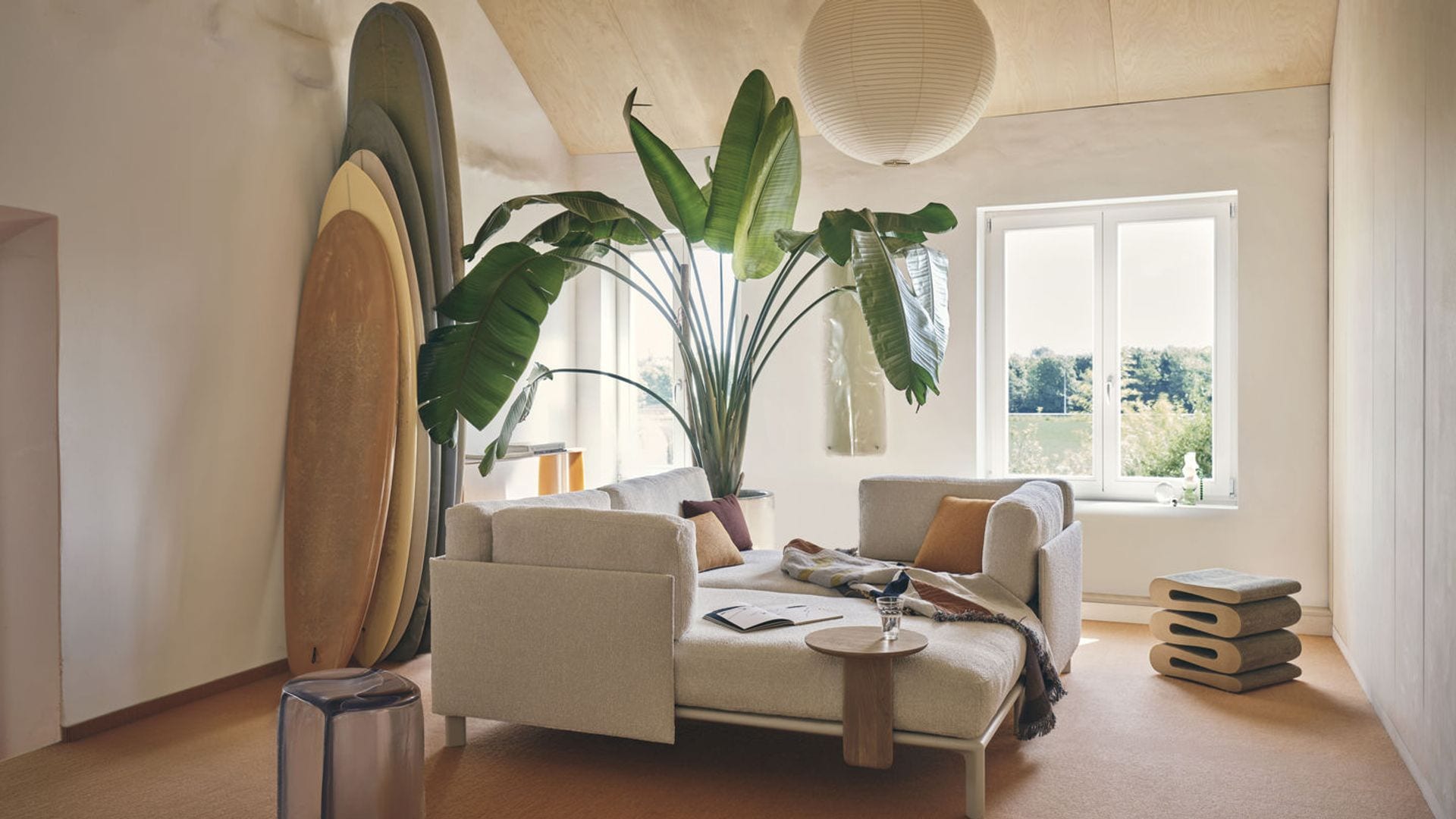 Salón con ventanas sin cortinas con vistas al jardín, carpintería blanca, lámpara de techo de papel, moqueta, sofá modular beige en forma de cama
