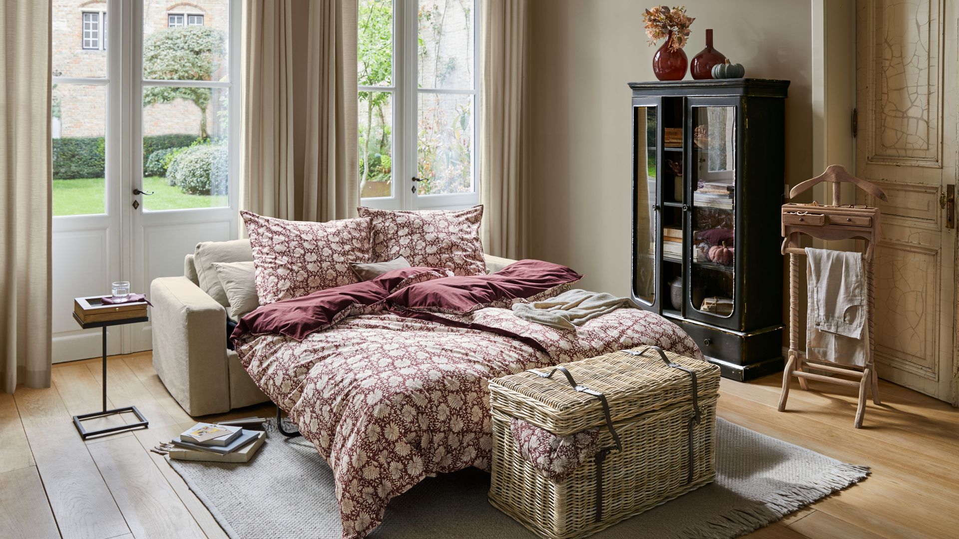 Dormitorio con gran ventanal, vitrina, suelo de madera, alfombra, cortinas, cesto a los pies de la cama, galán de noche