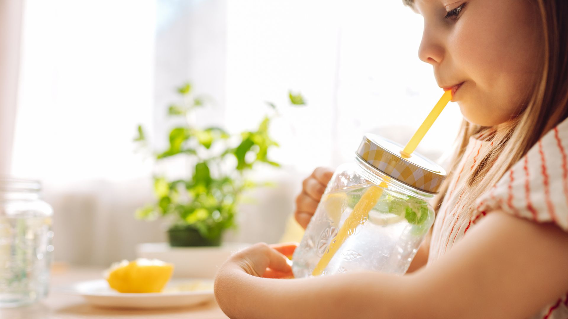 Niña bebiendo una limonada en un vaso de cristal con una pajita amarilla, con ropa de verano.