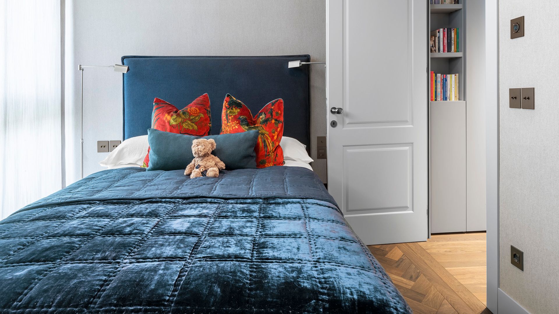 habitación infantil con cabecero tapizado en azul eléctrico, cojines rojos, colcha azul a juego, puerta de paso lacada en blanco