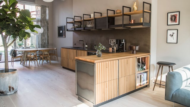 Cocina abierta con península de madera, estanterías metálicas en lugar de armarios superiores, mesa de comedor, planta y lámpara de techo