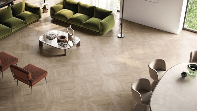 Salón comedor con suelo porcelánico que imita la madera, sofás verdes, mesa de centro, cuadro en la pared y butacas marrones 