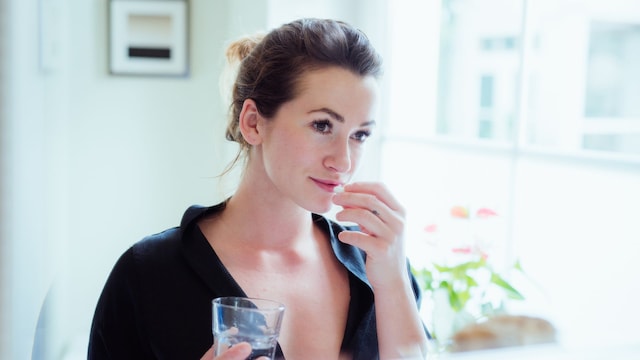 Mujer tomando vitaminas y suplementos alimenticios frente al espejo