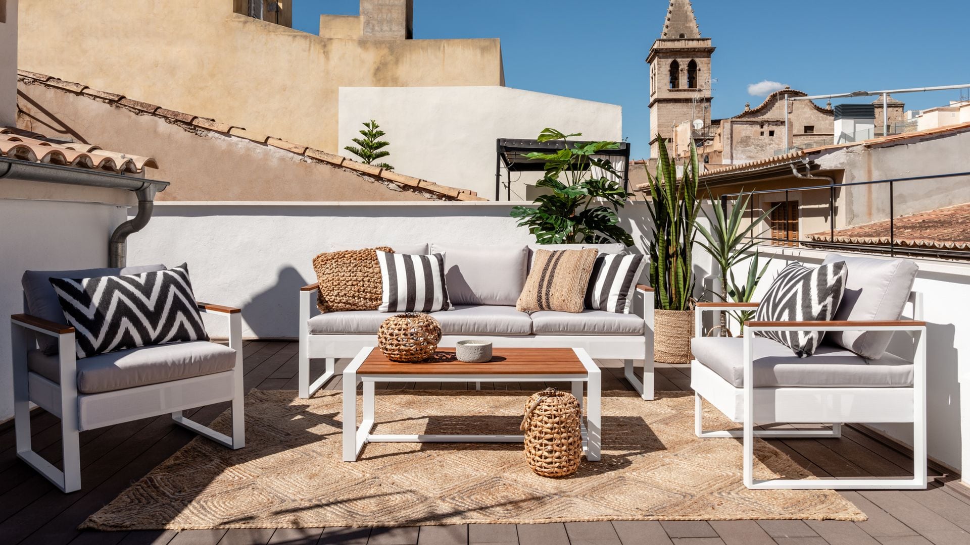 Terraza en una azotea con estar con muebles blancos, alfombra de fibras vegetales, plantas, cojines de rayas