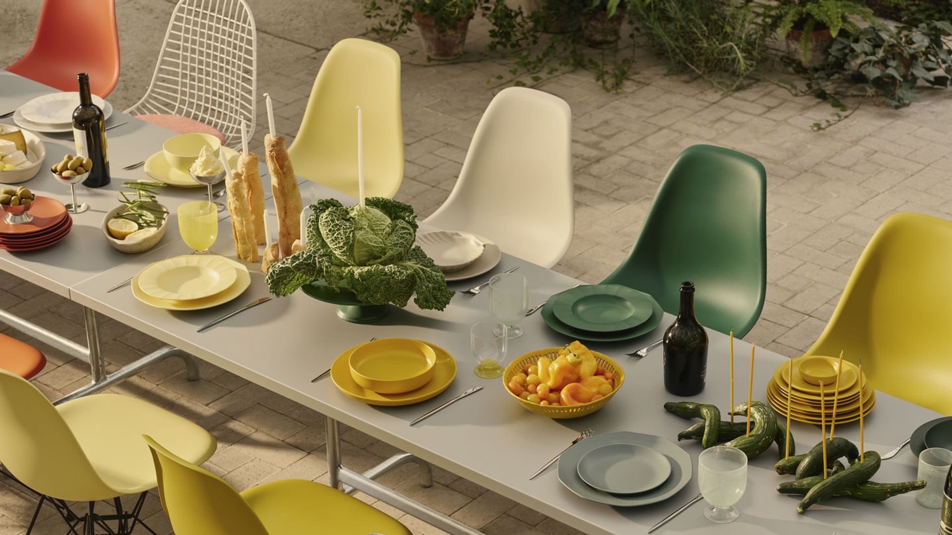 Mesa de comedor exterior con vajilla verde y amarillo, sillas de los Eames en verde, amarillo, blanco y mostaza 