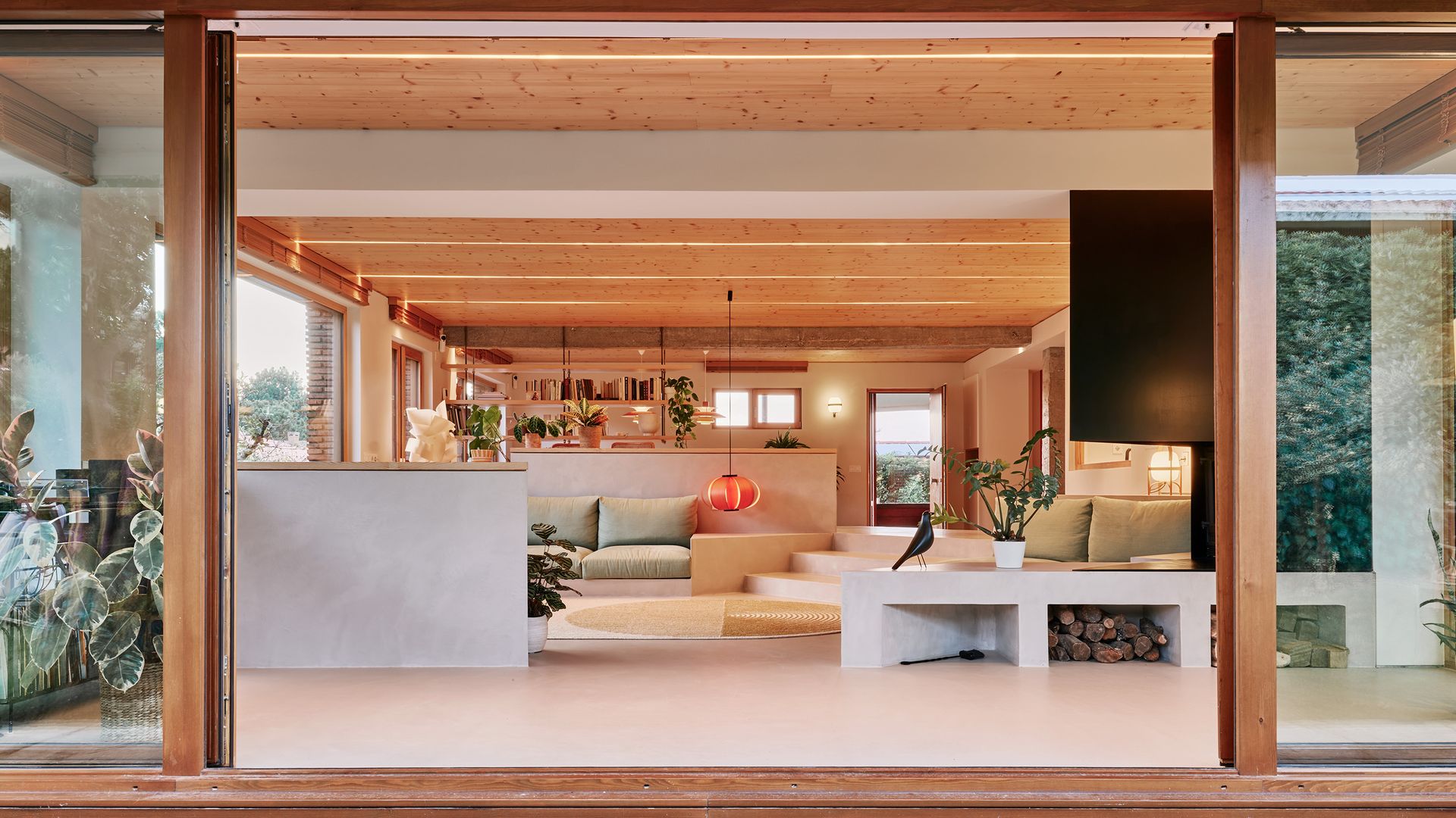 Salón visto desde el jardín con gran ventanal corredero de madera, techo de madera 