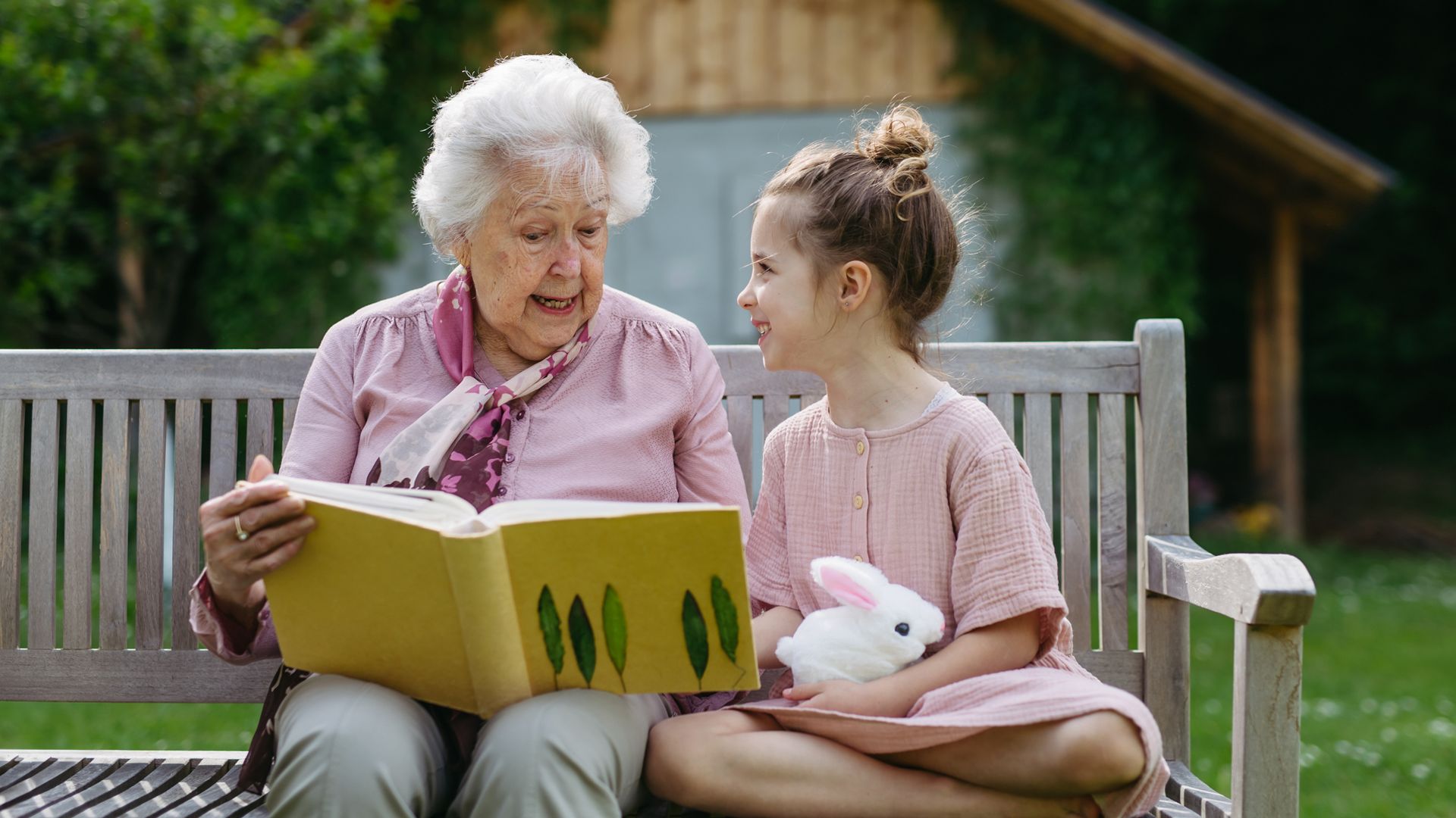 abuela con su nieta sentada en un banco, leyendo un libro