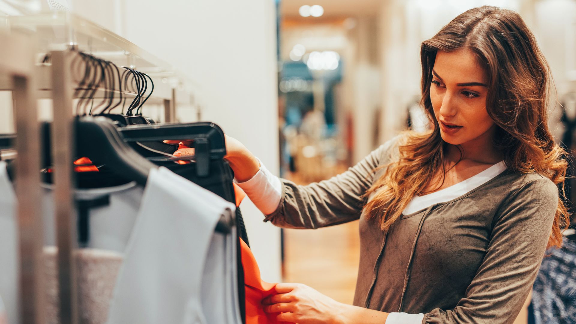 Mujer joven de pelo castaño mirando ropa en un centro comercial