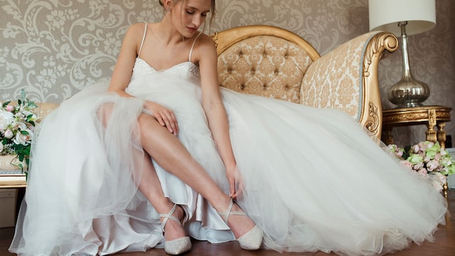 Mujer vestida de novia poniéndose unos zapatos con brillo y tiras cruzadas al tobillo