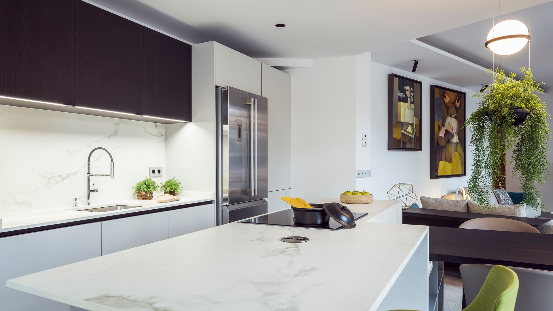 Cocina abierta con isla, encimera blanca, antepecho a juego, planta colgante