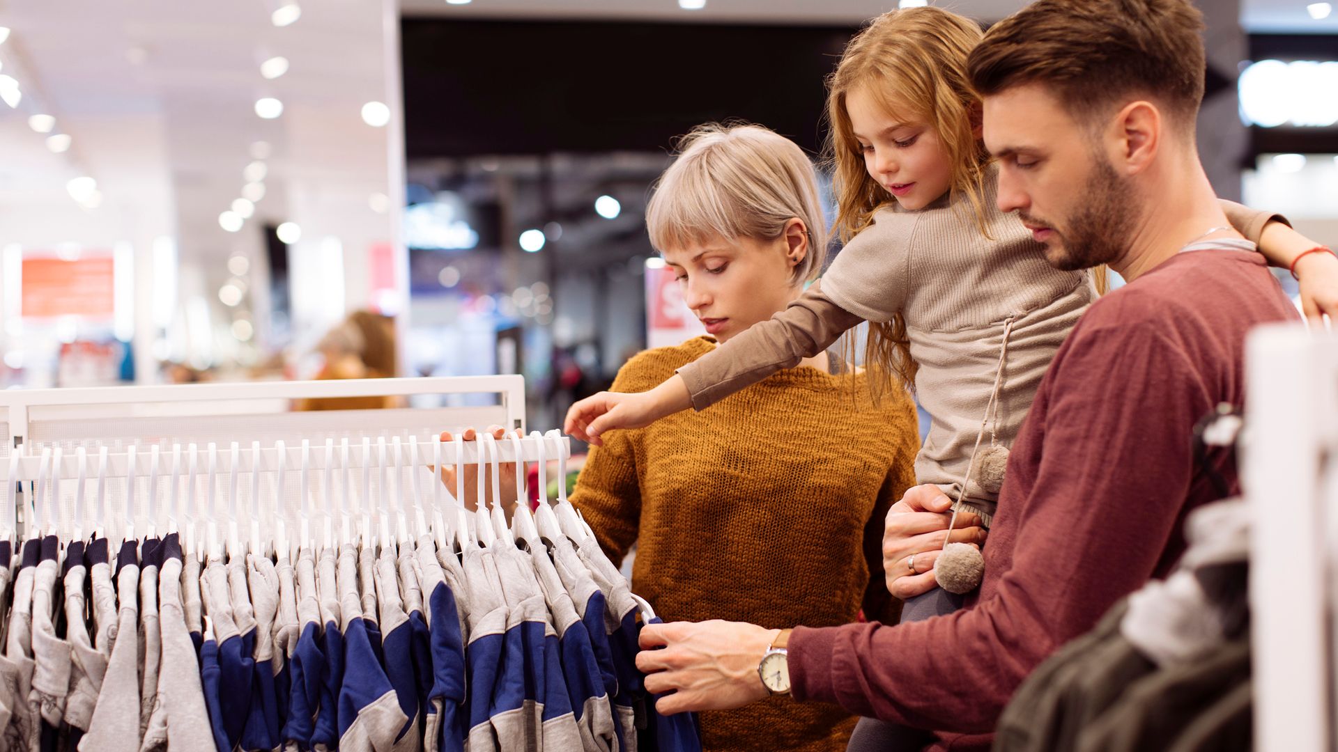 Familia comprando ropa en una tienda, con la niña en brazos.