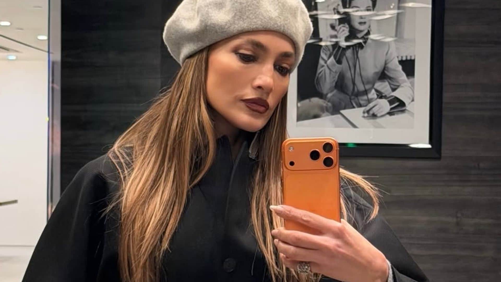 Jennifer Lopez con boina gris, labios marrones y manicura afterglow, en un look parisino contemporáneo.