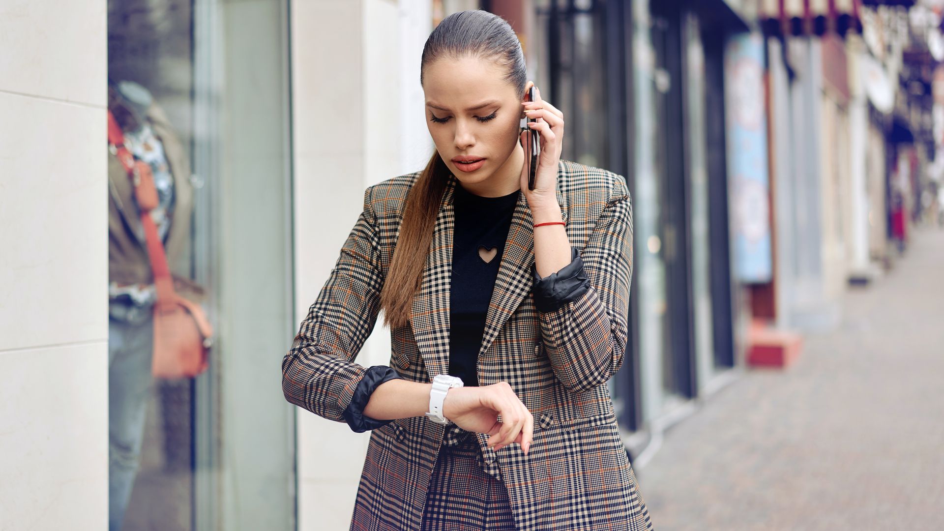 Mujer preocupada y estresada chequeando su reloj mientras habla por teléfono 