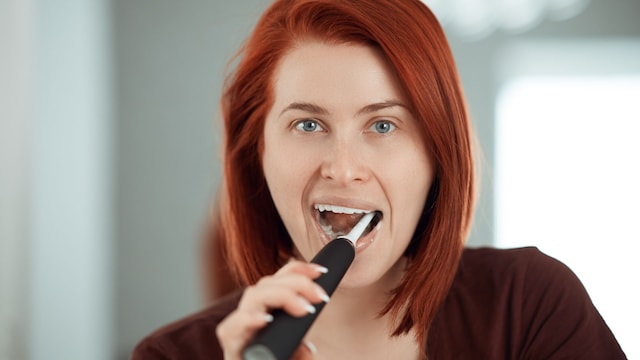 Una chica cepillándose los dientes con un cepillo eléctrico