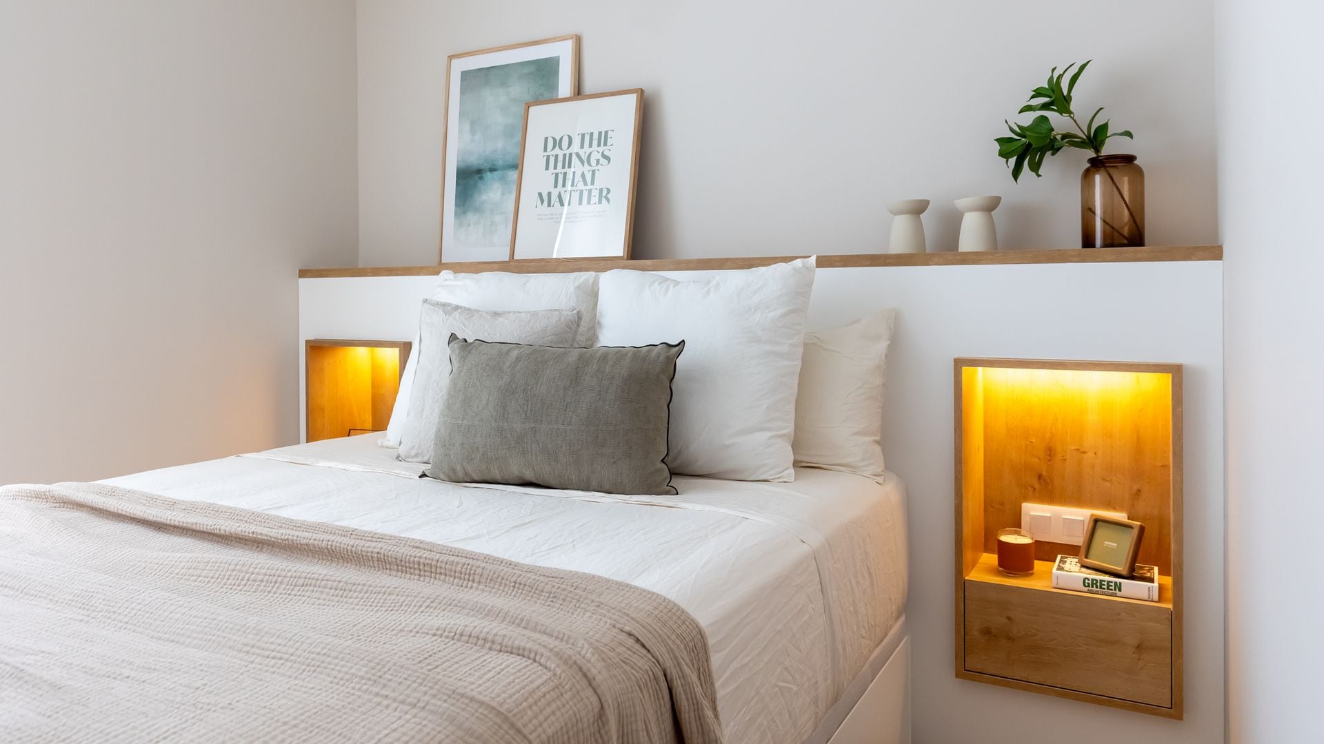 Dormitorio de obra con mesitas de noche integradas, con luz interior, repisa con cuadros, jarrones, cojines sobre la cama 