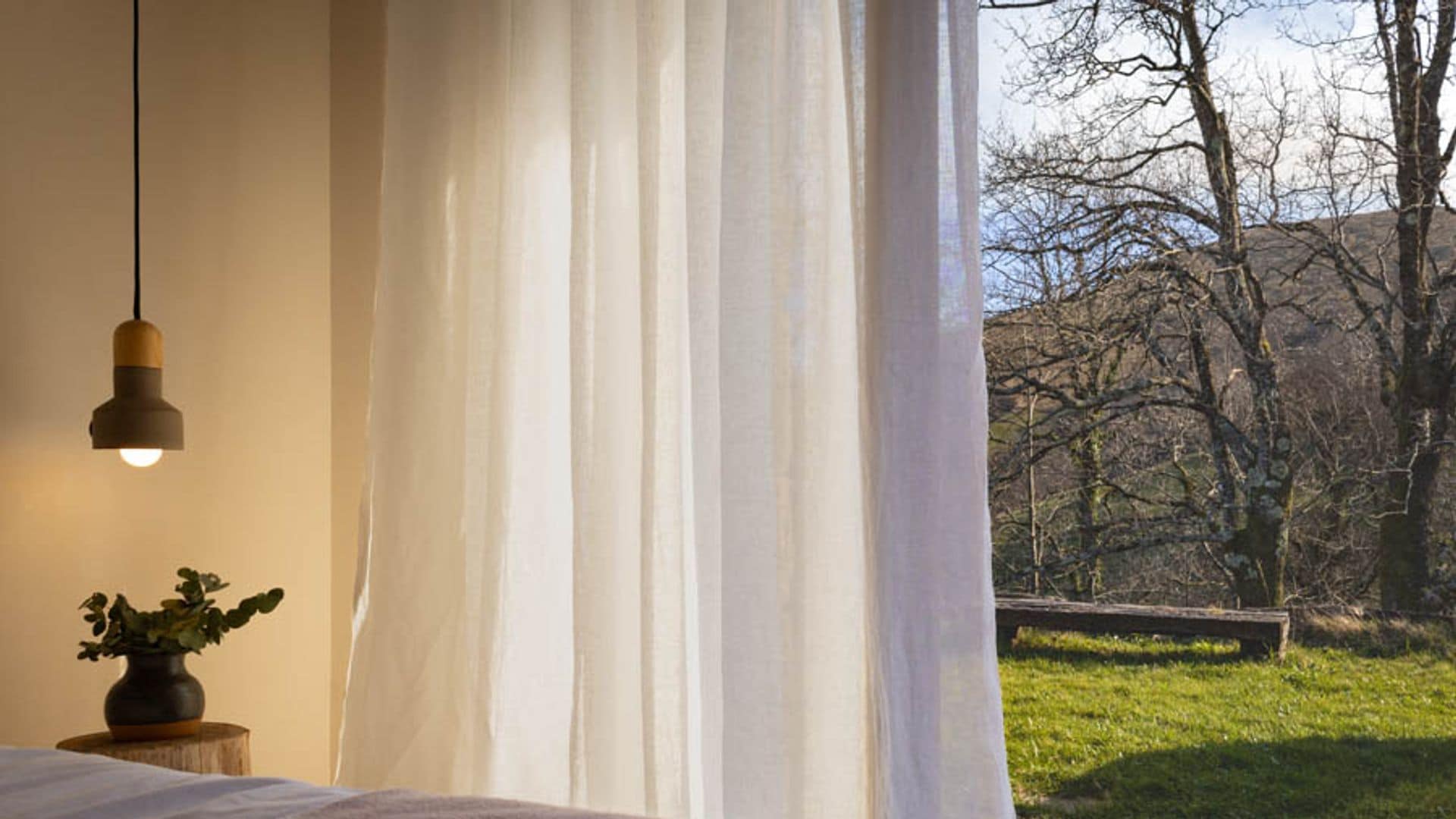 Dormitorio con cortinas blancas con salida al jardín, lámpara de techo y jarrón en la mesita de noche