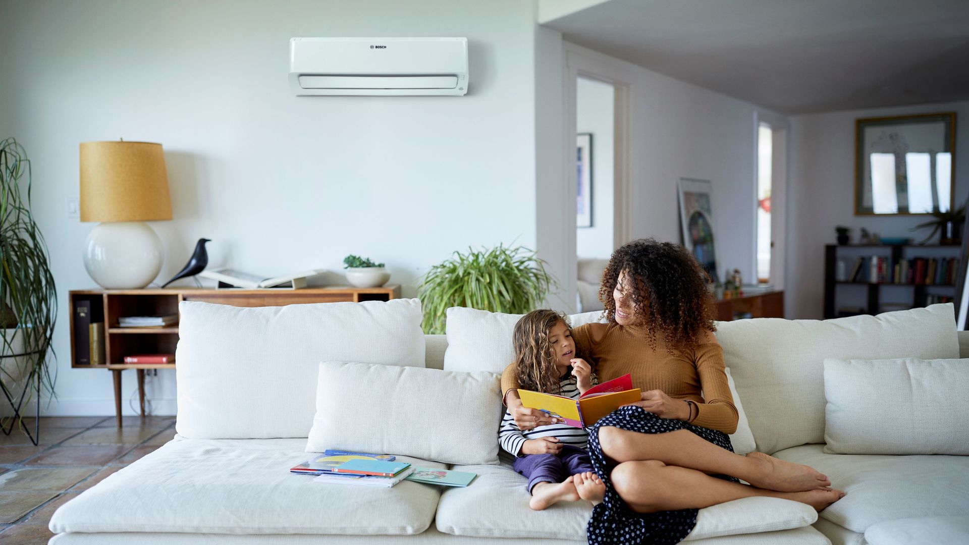 Salón con sofá blanco, madre e hija y split de aire acondicionado 