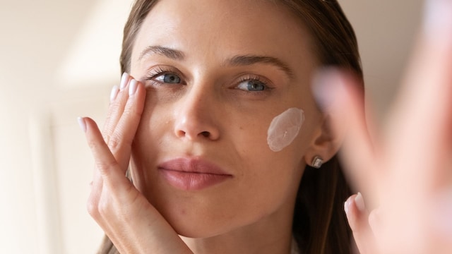 Mujer joven aplicándose crema facial en el rostro frente a un espejo