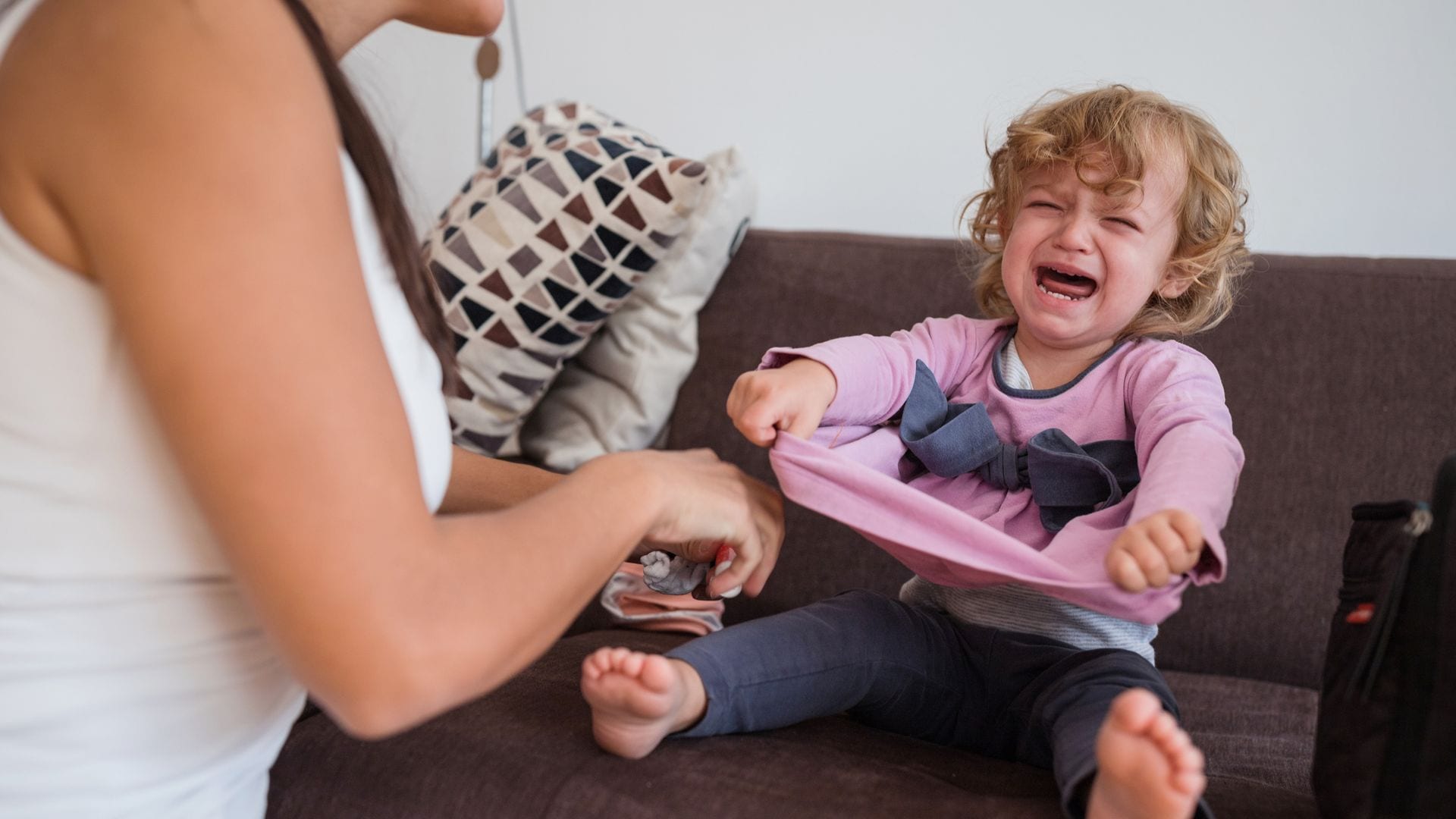 Madre intenta vestir a su hija, que está en medio de una rabieta