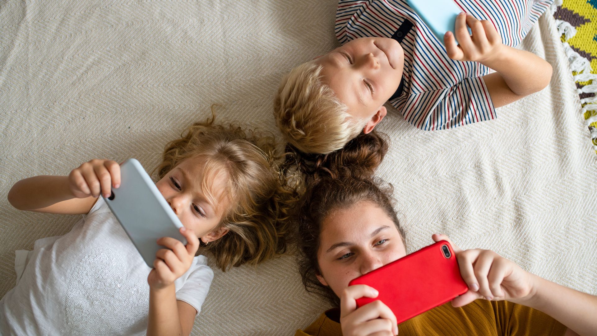 Niños tumbados en el suelo mirando sus teléfonos móviles