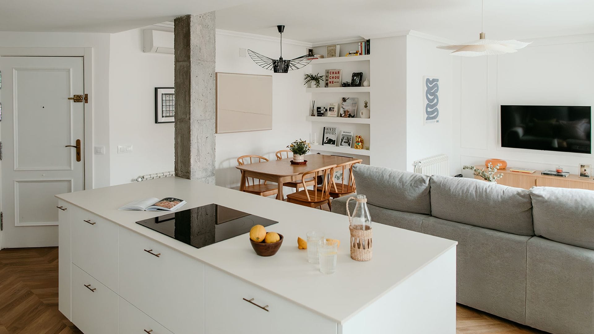 Recibidor abierto a cocina, salón y comedor con isla blanca, columna de hormigón y campana de techo