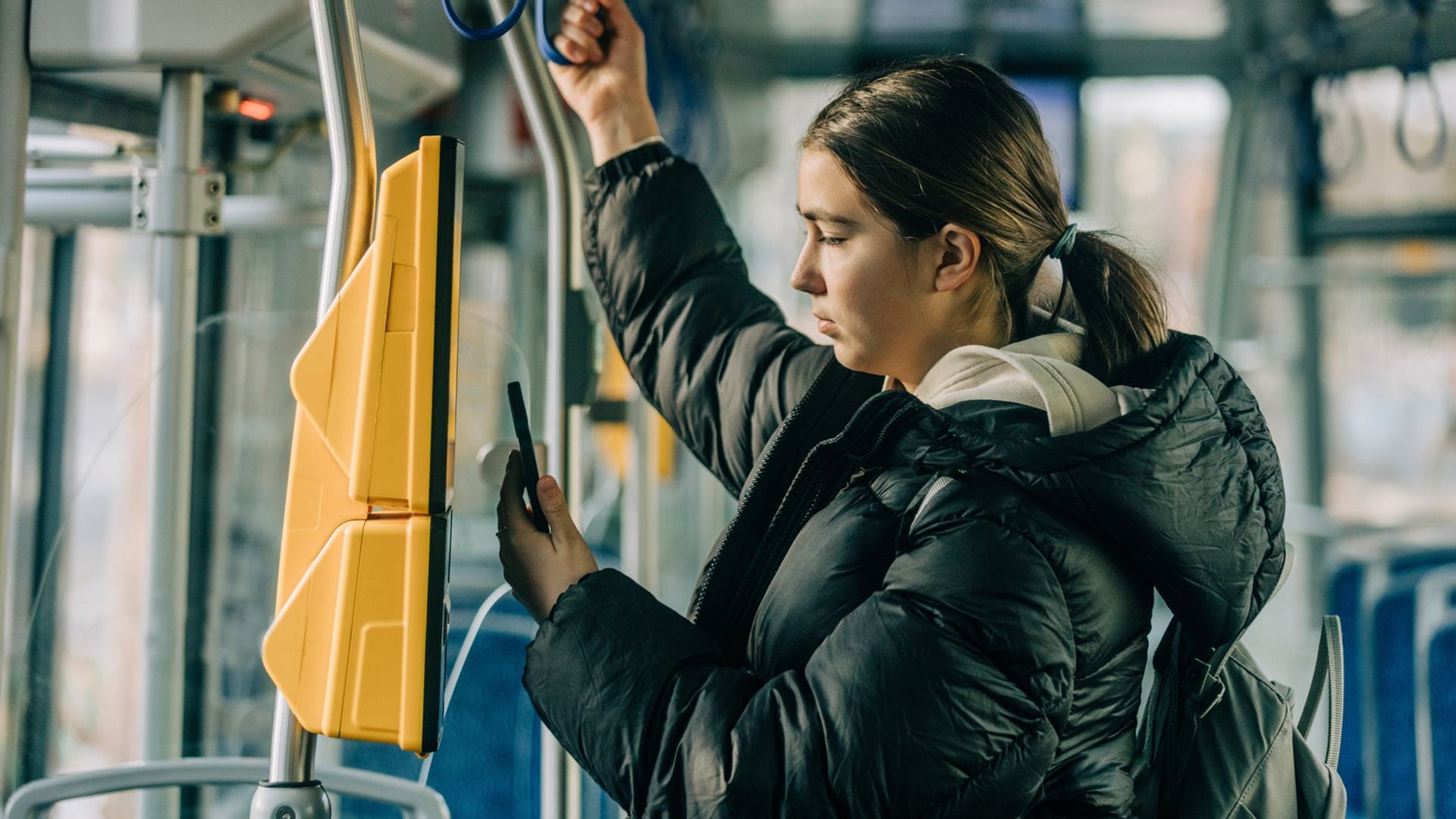 Chica subida en el autobús con su teléfono móvil en la mano