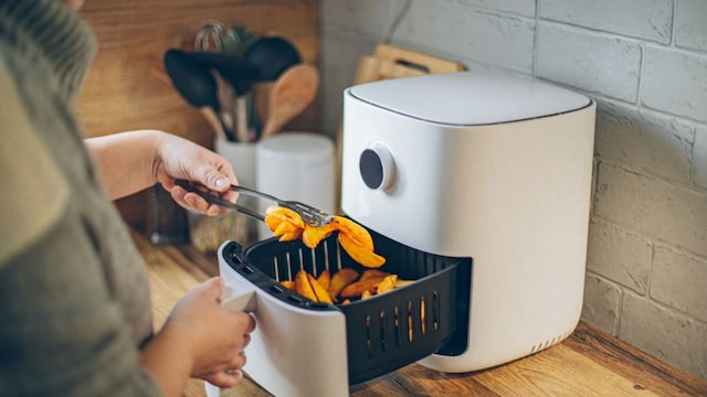 Una mujer cocinando patatas en una freidora de aire