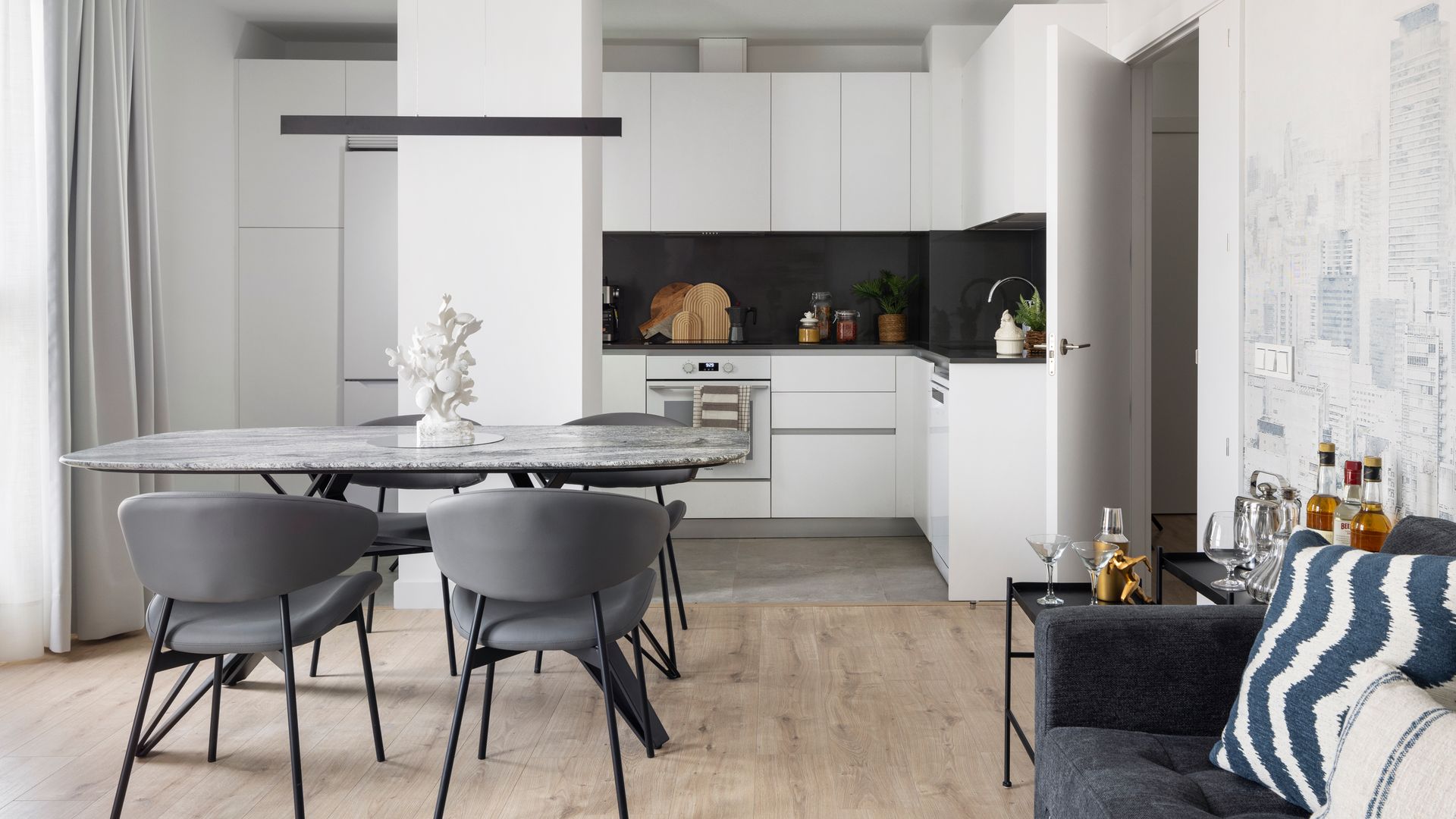 Cocina blanca abierta con comedor, antepecho negro, sofá gris, papel pintado