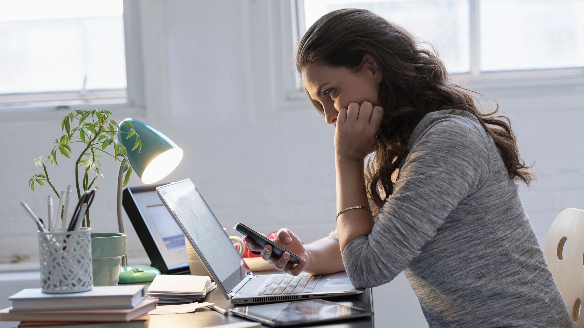 Mujer mirando el móvil y el ordenador portátil 
