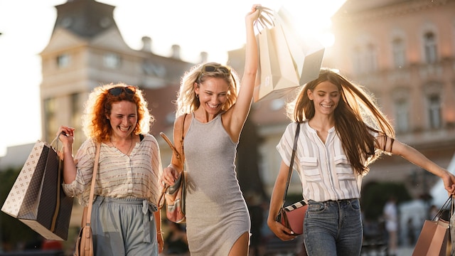 Grupo de chicas con bolsas de la compra paseando por la calle muy felices en un tiempo veraniego, al atardecer.