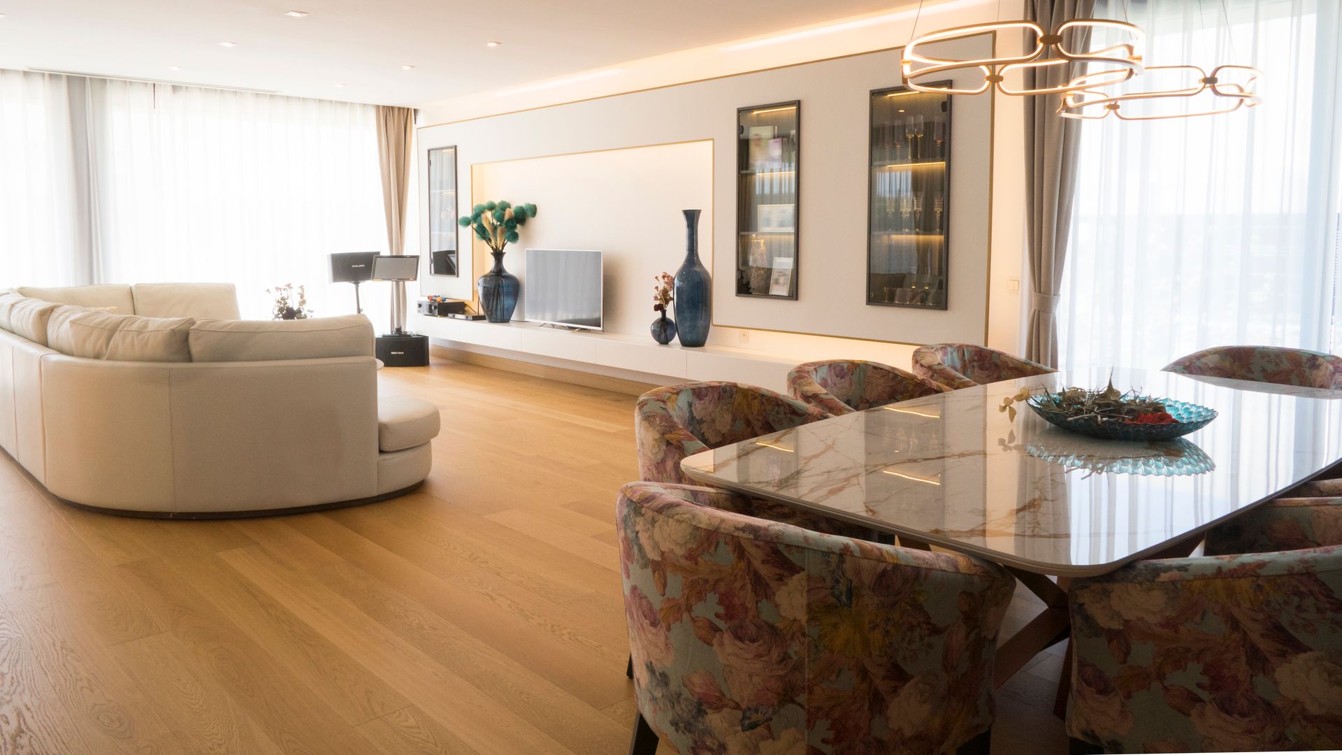 Salón comedor con mueble a medida, suelo de madera, mesa rectangular, sillas tapizadas y lámparas de techo