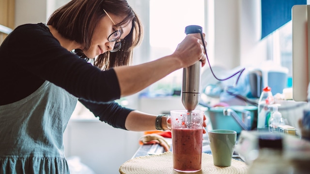 Mujer haciendo un batido de frutas con su batidora de mano en la cocina