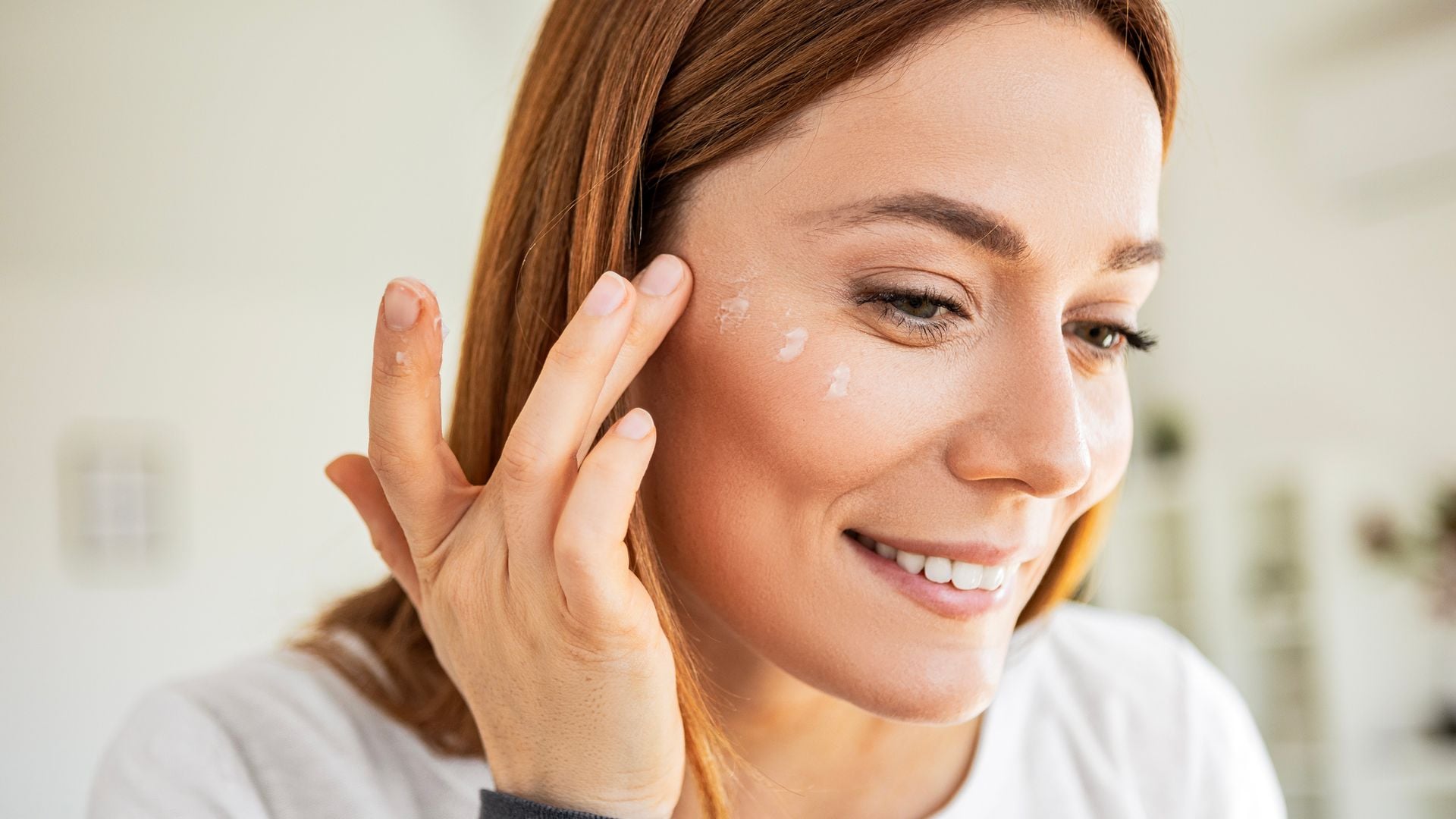 Rostro de mujer de 40 años aplicándose crema en las mejillas