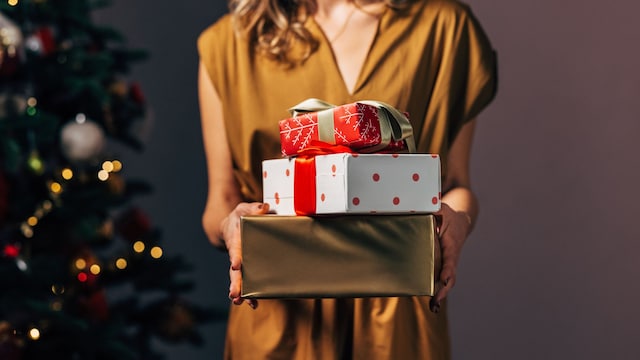 Mujer con regalos de Navidad en primer plano con vestido de fiesta y árbol de Navidad