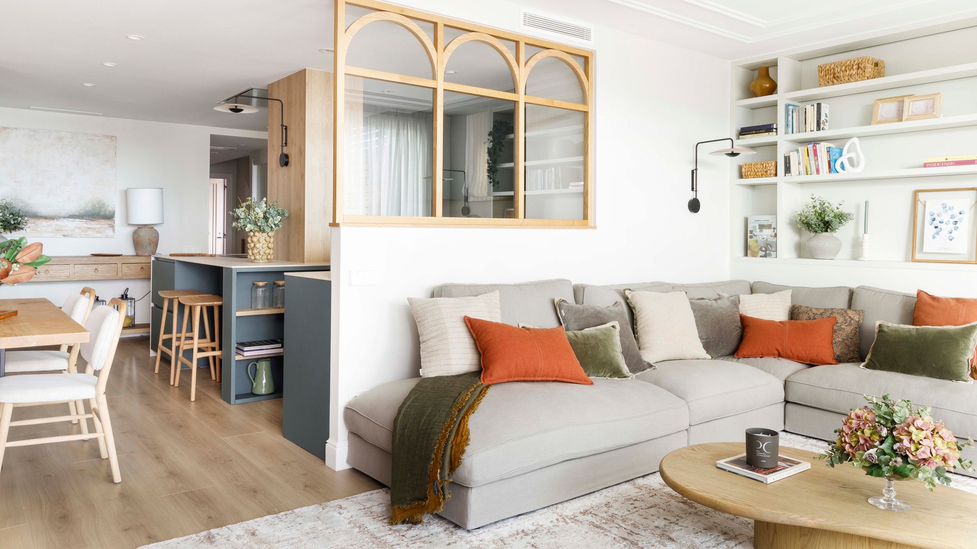 Salón comedor y cocina, con sofás grises, tabique de cristal con arcos de madera para separar cocina de salón
