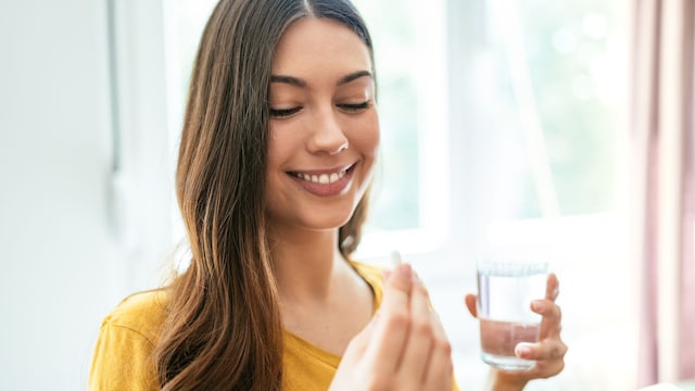 Mujer joven tomándose un suplemento alimenticio con un vaso de agua sonriendo