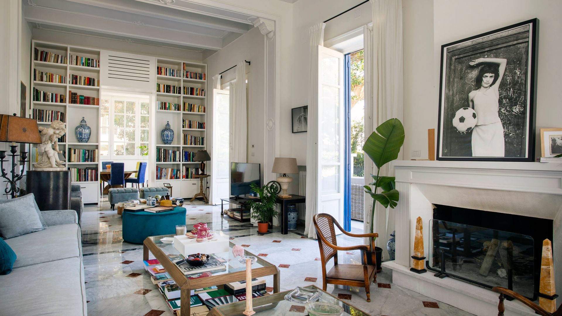 Salón con chimenea con foto en blanco y negro sobre la repisa, suelo porcelánico, mesas de centro con el sobre de cristal, sofá blanco y estantería blanca
