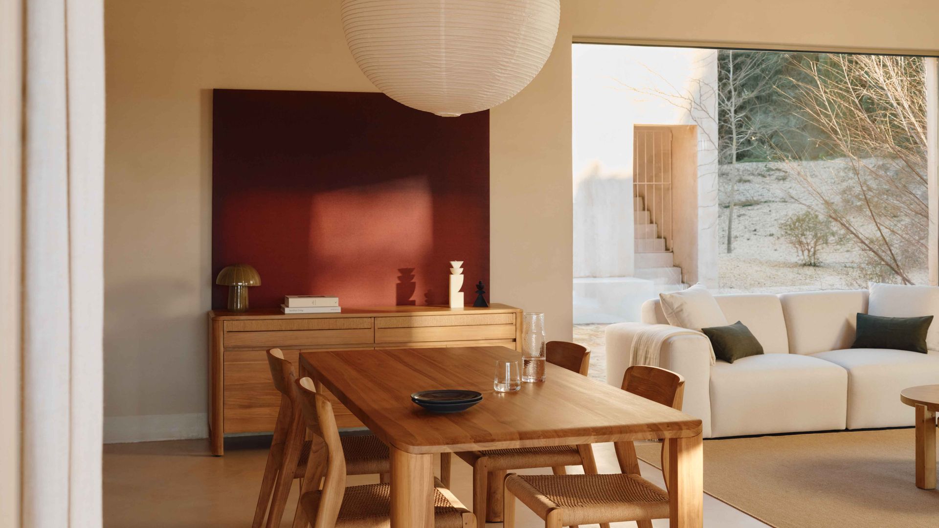 Salón comedor con sofá blanco, mesa de comedor de madera, sillas de madera, lámpara de papel, ventanal