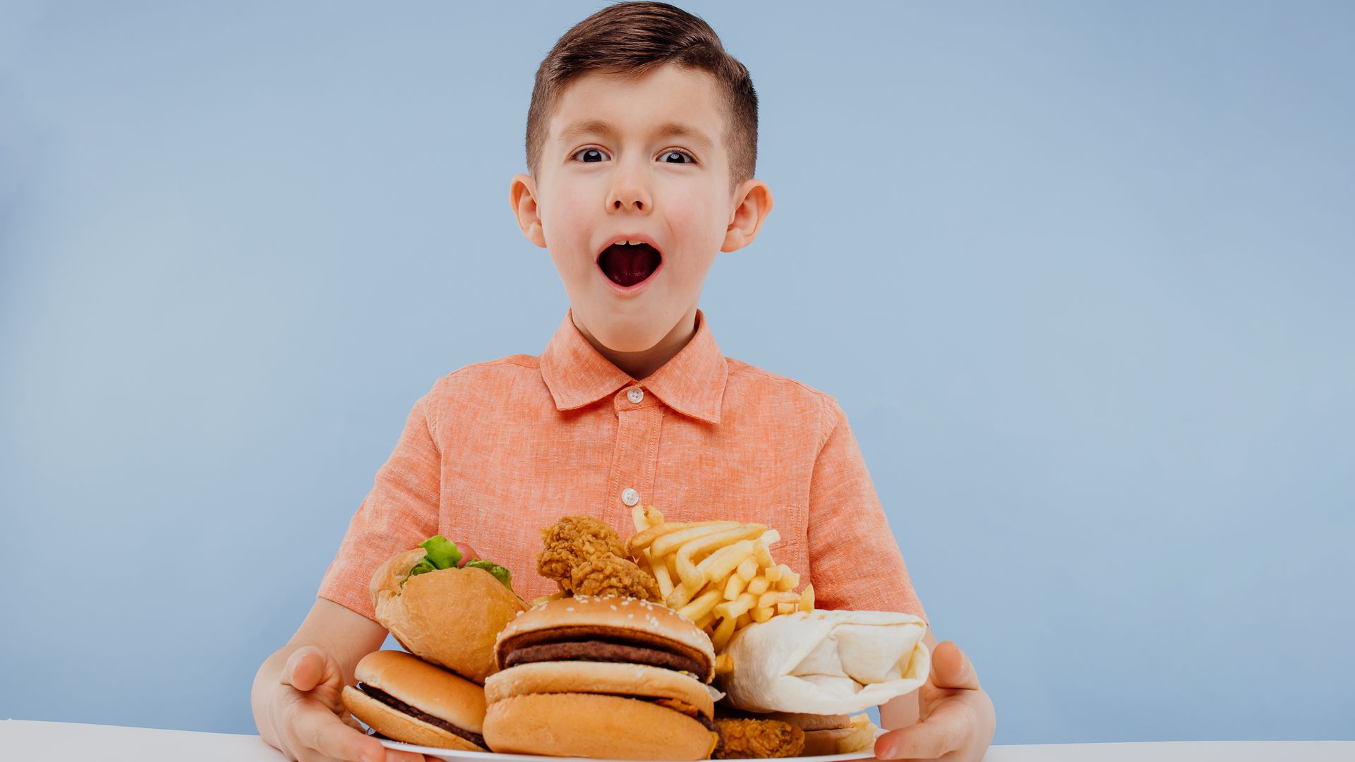 Niño delante de un plato con hamburguesas, patatas y otros ultraprocesados