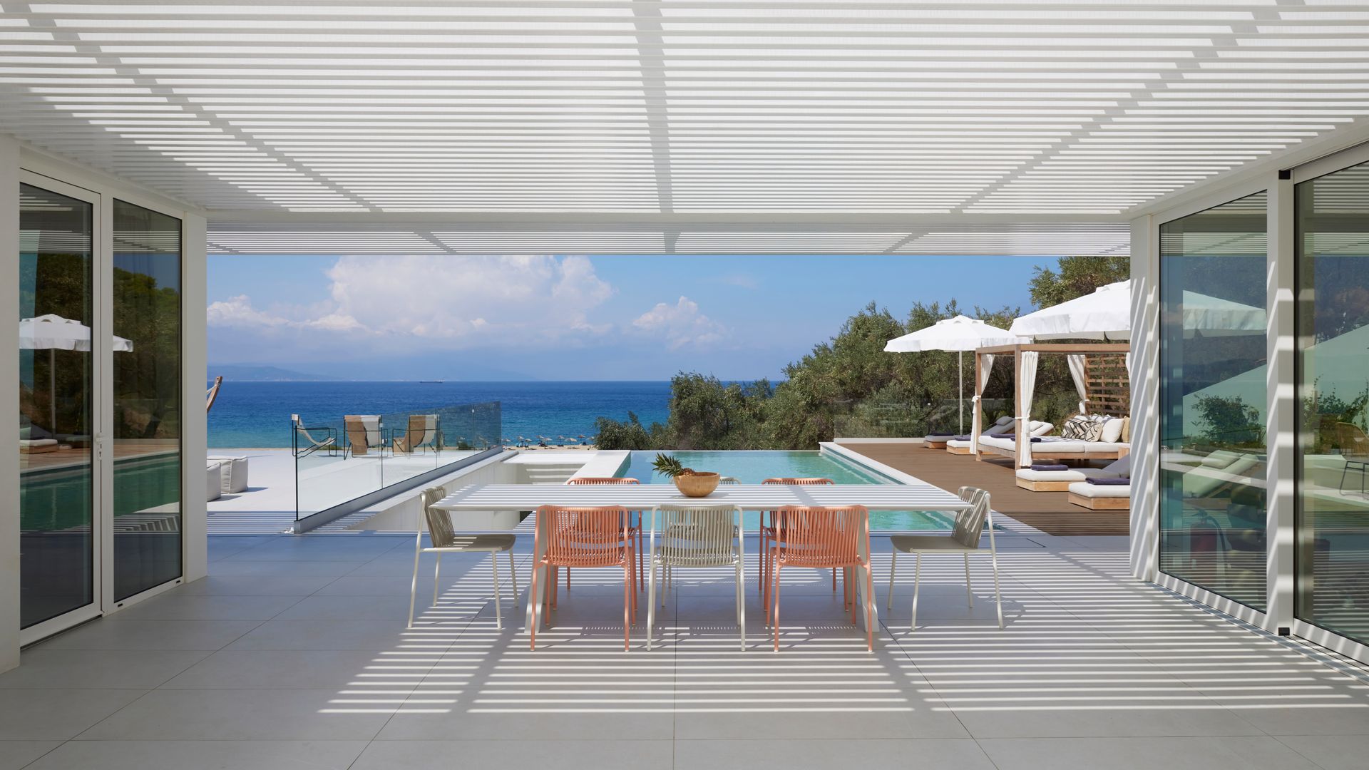 Comedor exterior bajo una pérgola, sillas de comedor de rafia sintética de colores, piscina infinita, vistas al mar, sombrillas con hamacas 