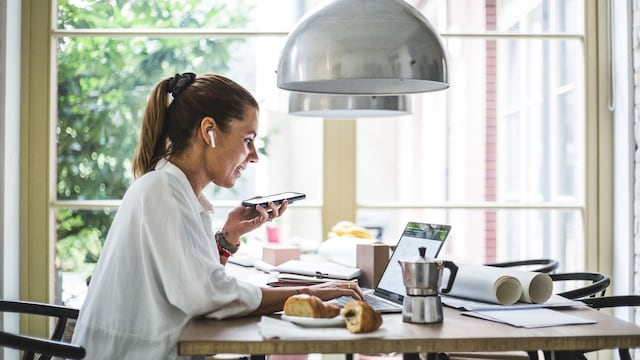 mujer desayunando mientras trabaja con su portátil y habla por teléfono