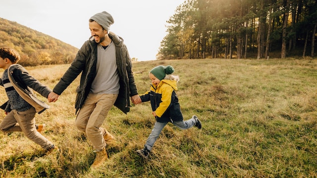 Padre con dos hijos en la naturaleza, corriendo por el bosque en otoño-invierno